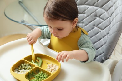 Cute little baby eating healthy food in high chair indoors