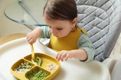 Photo of Cute little baby eating healthy food in high chair indoors