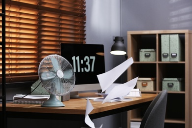 Photo of Modern electric fan and flying paper in office