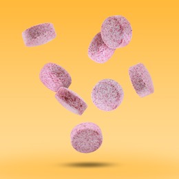 Image of Vitamin. Pink tablets falling on orange gradient background