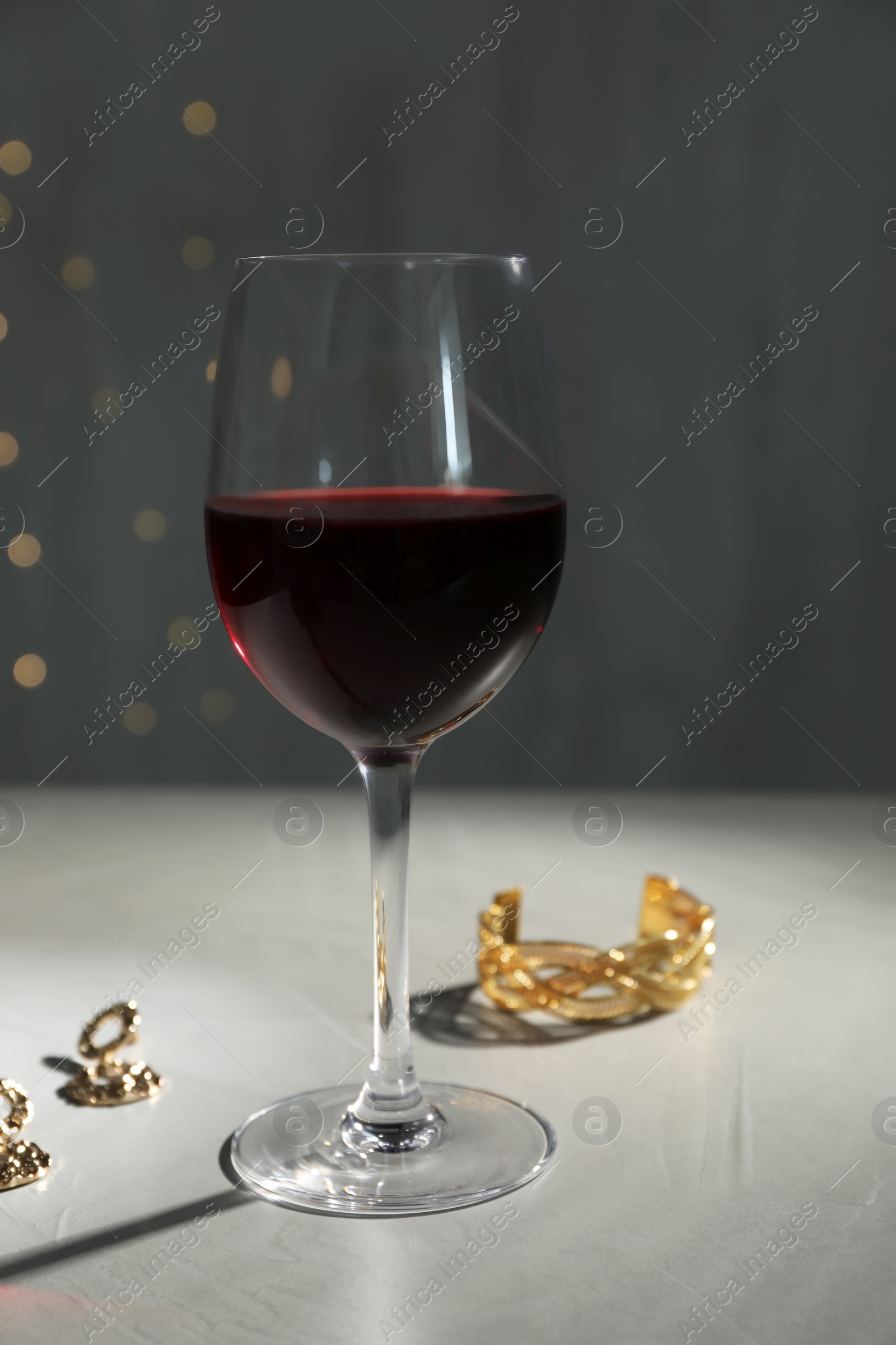 Photo of Glass of red wine and jewelry on white table against blurred festive lights
