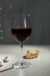 Glass of red wine and jewelry on white table against blurred festive lights