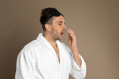 Sleepy young man in bathrobe on brown background