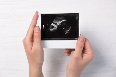 Photo of Woman holding ultrasound photo of baby over table, top view