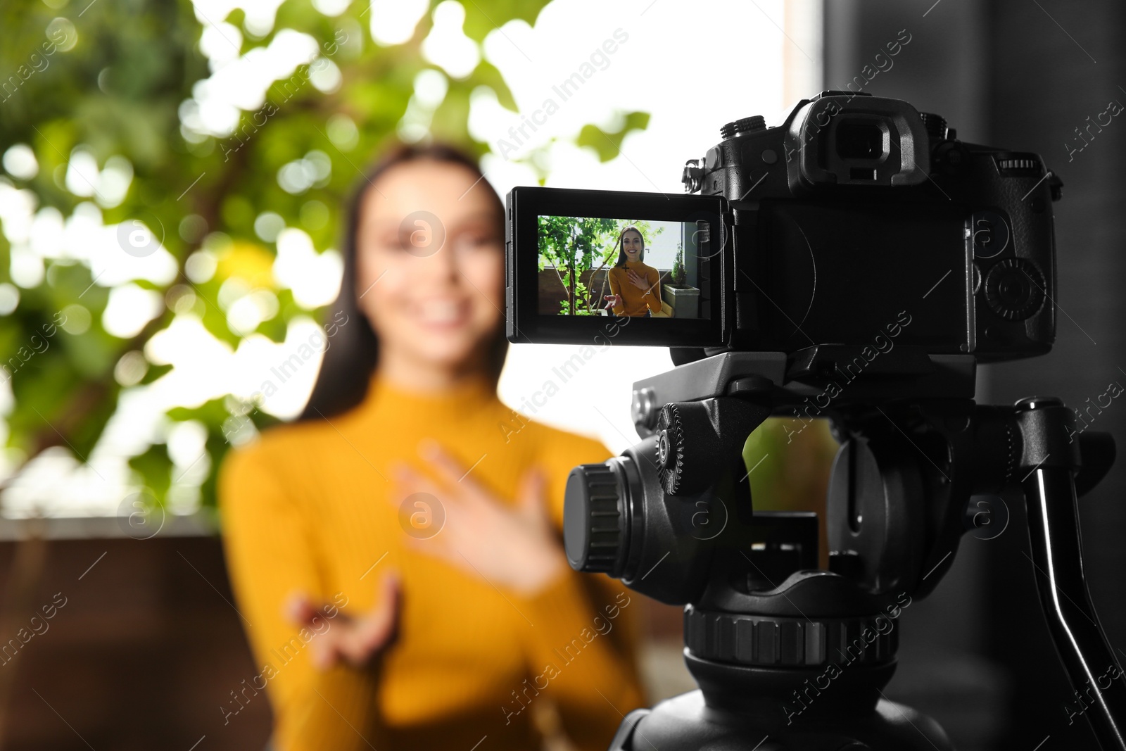 Photo of Young blogger recording video indoors, focus on camera screen