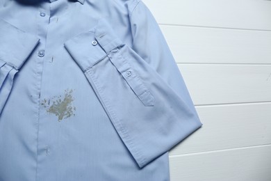 Photo of Light blue shirt with stain on white wooden table, above view. Space for text