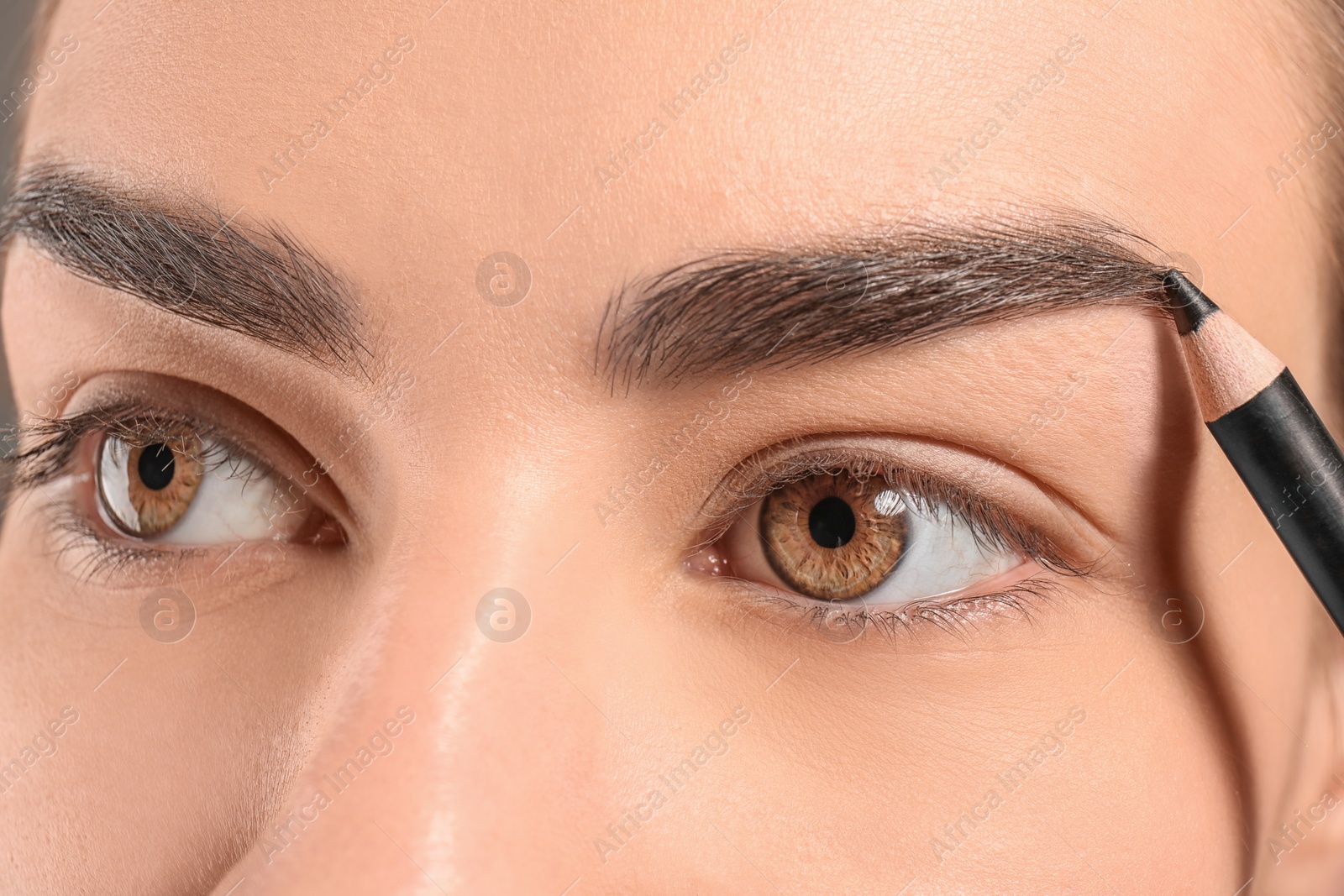 Photo of Young woman correcting eyebrow shape with pencil, closeup