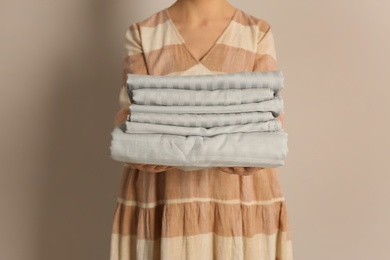 Photo of Woman holding stack of clean bed linens on beige background