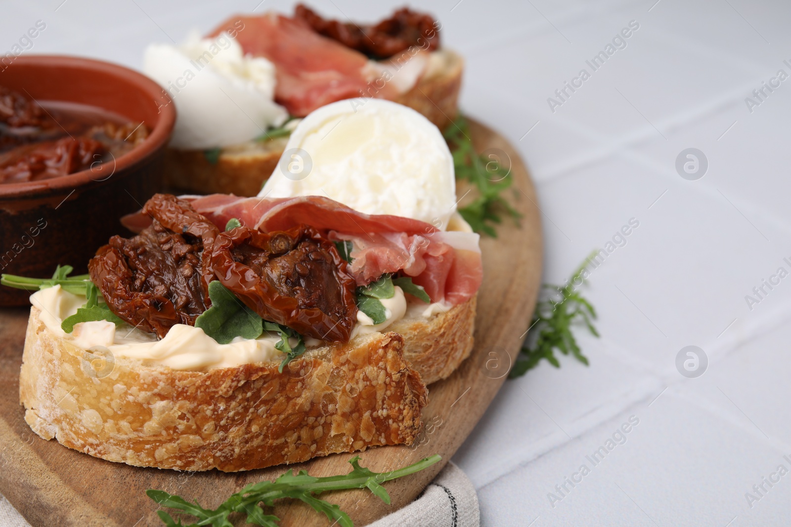 Photo of Delicious sandwiches with burrata cheese, ham and sun-dried tomatoes served on white tiled table, closeup. Space for text