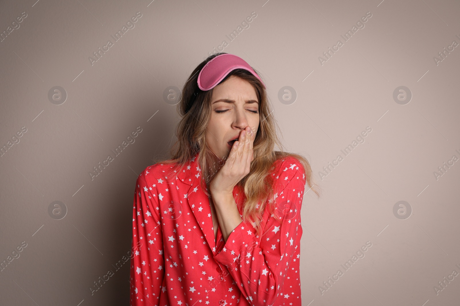 Photo of Young tired woman with sleeping mask yawning on beige background