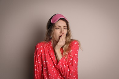 Young tired woman with sleeping mask yawning on beige background