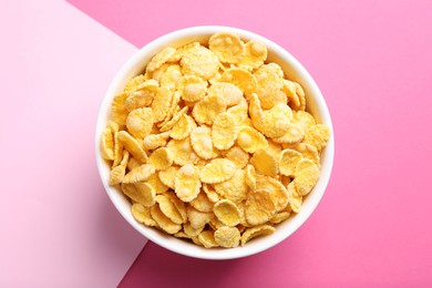 Photo of Bowl of tasty crispy corn flakes on pink background, top view