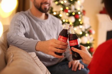 Photo of MYKOLAIV, UKRAINE - JANUARY 27, 2021: Young couple holding bottles of Coca-Cola in room decorated for Christmas, closeup
