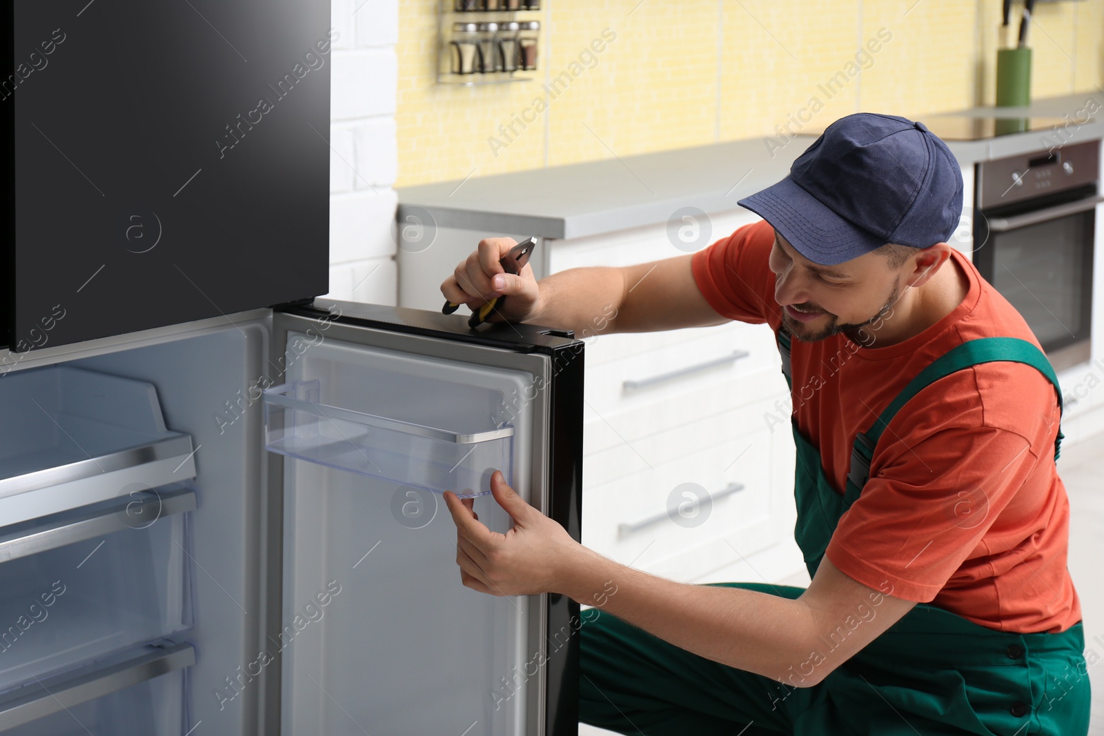 Photo of Male technician with pliers repairing refrigerator indoors