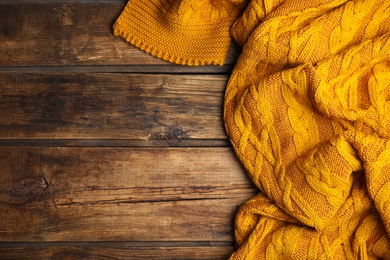 Orange knitted plaid on wooden table, top view. Space for text