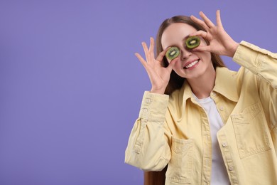 Photo of Young woman holding halves of kiwi near her eyes on purple background. Space for text