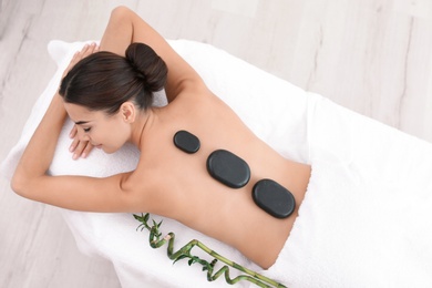 Photo of Beautiful young woman getting hot stone massage in spa salon, top view