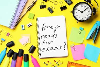 Photo of Notebook with phrase Are You Ready For Exams and stationery on yellow background, flat lay