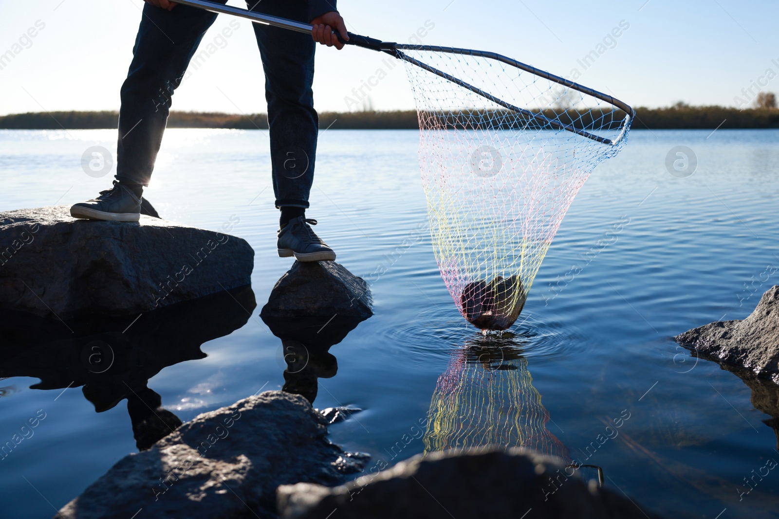 Photo of Fisherman holding fishing net with catch at riverside, closeup