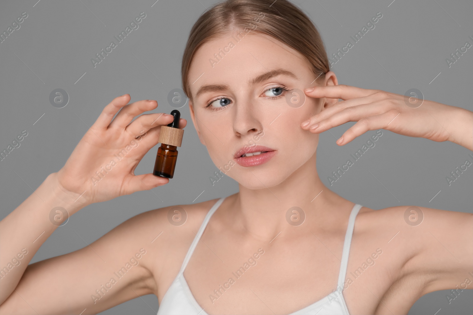 Photo of Beautiful young woman with bottle of essential oil on light grey background