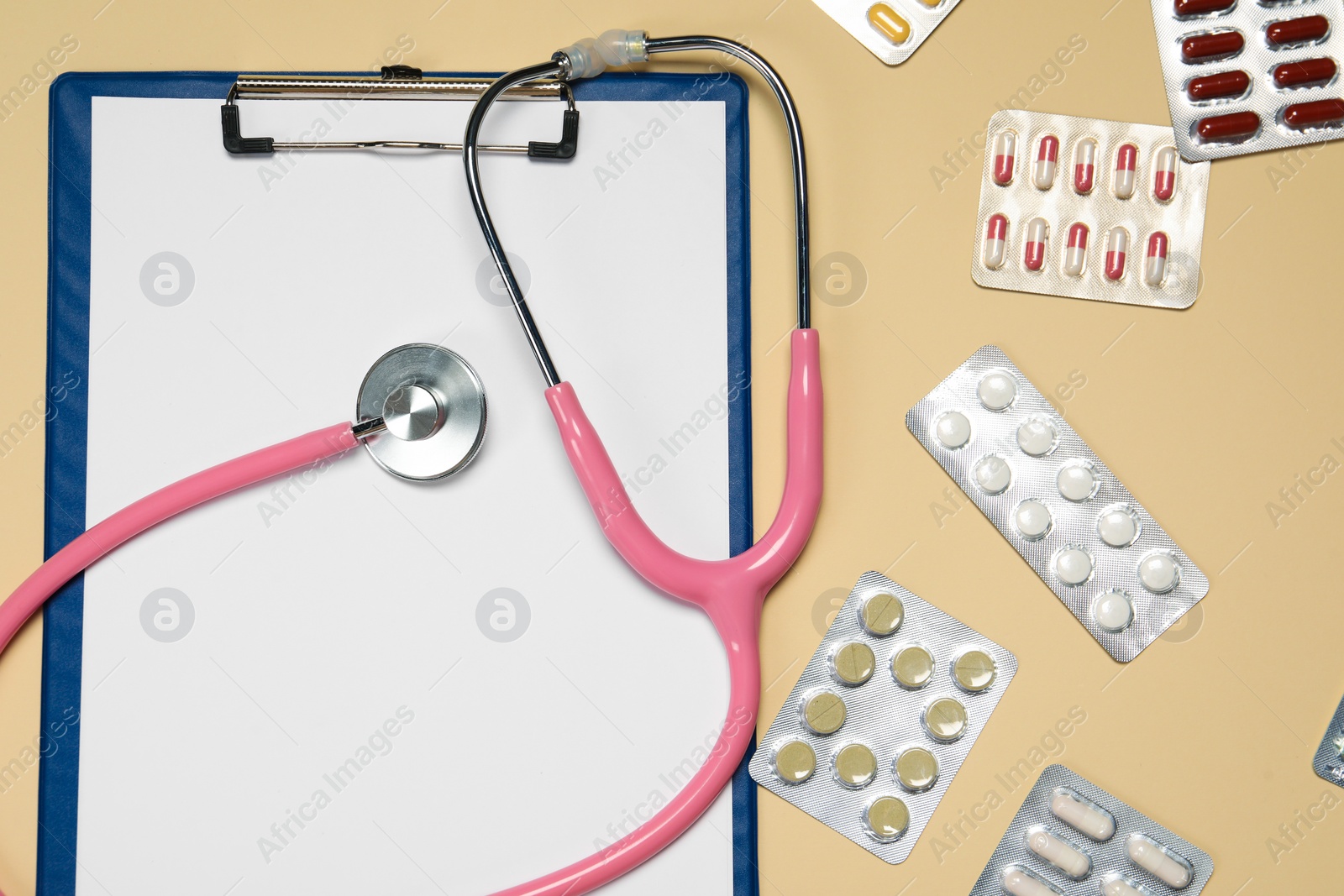 Photo of Stethoscope, clipboard and pills on beige background, flat lay. Medical tool