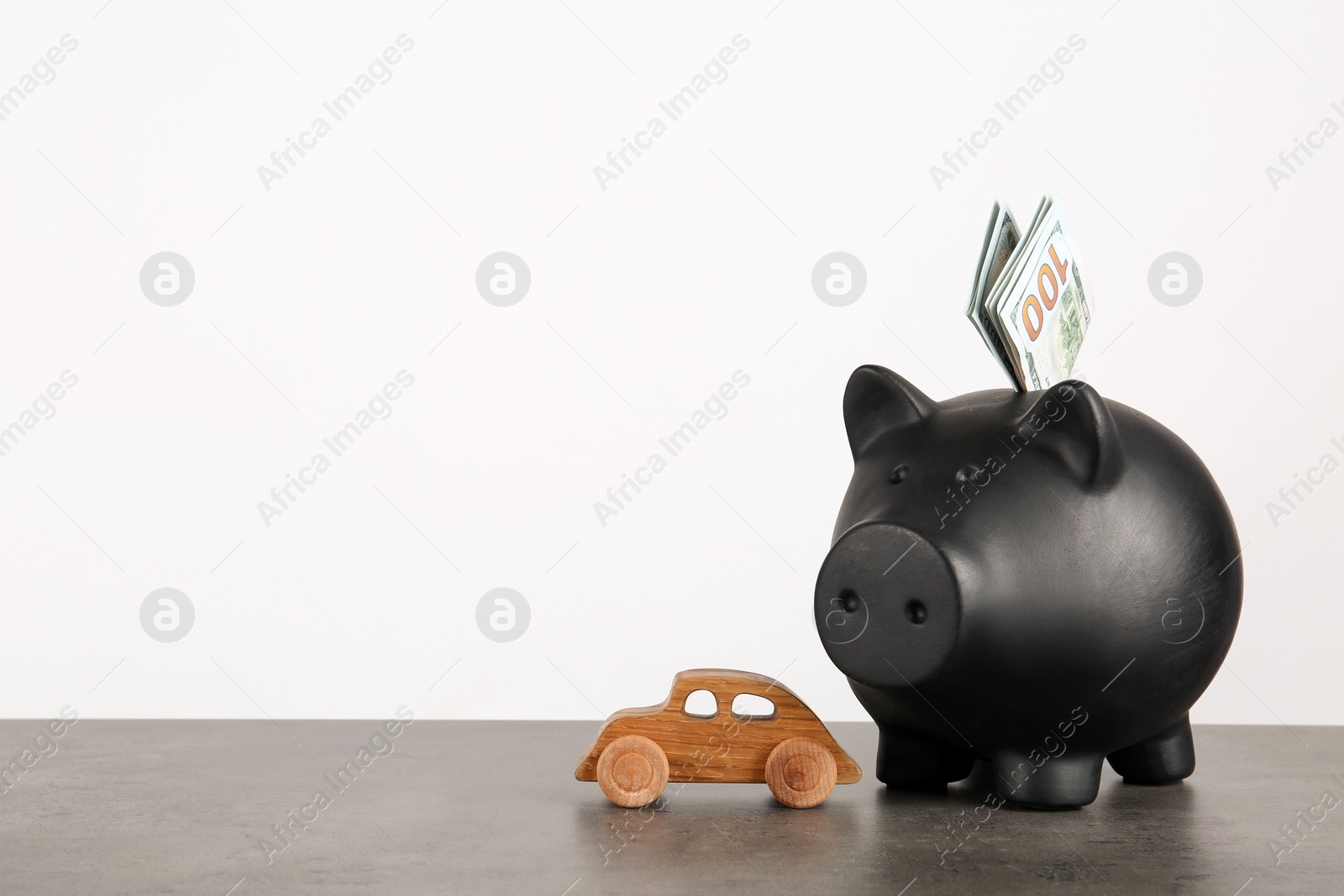 Photo of Piggy bank with dollar banknotes and toy car on table against white background. Space for text