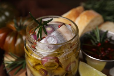 Tasty marinated fish with onion and rosemary in jar on blurred background, closeup