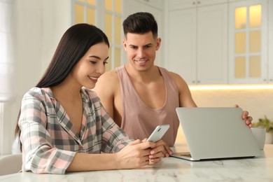 Happy couple wearing pyjamas with gadgets spending time together in kitchen