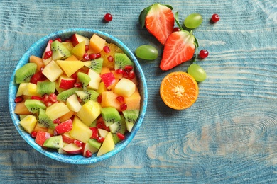Photo of Bowl with fresh cut fruits on wooden table, top view