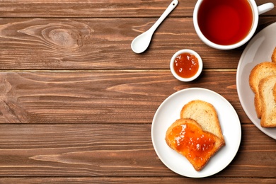 Photo of Toasts with jam and cup of tea on wooden background, flat lay