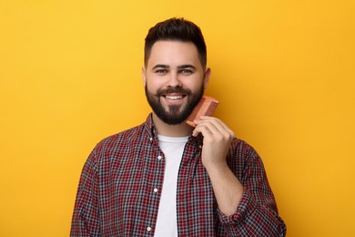 Handsome young man combing beard on yellow background