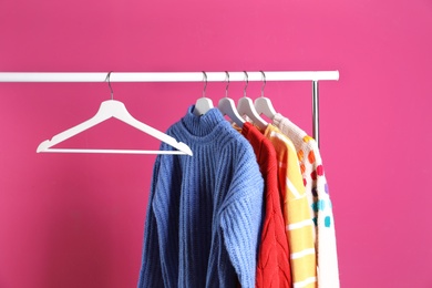 Photo of Collection of warm sweaters hanging on rack against color background