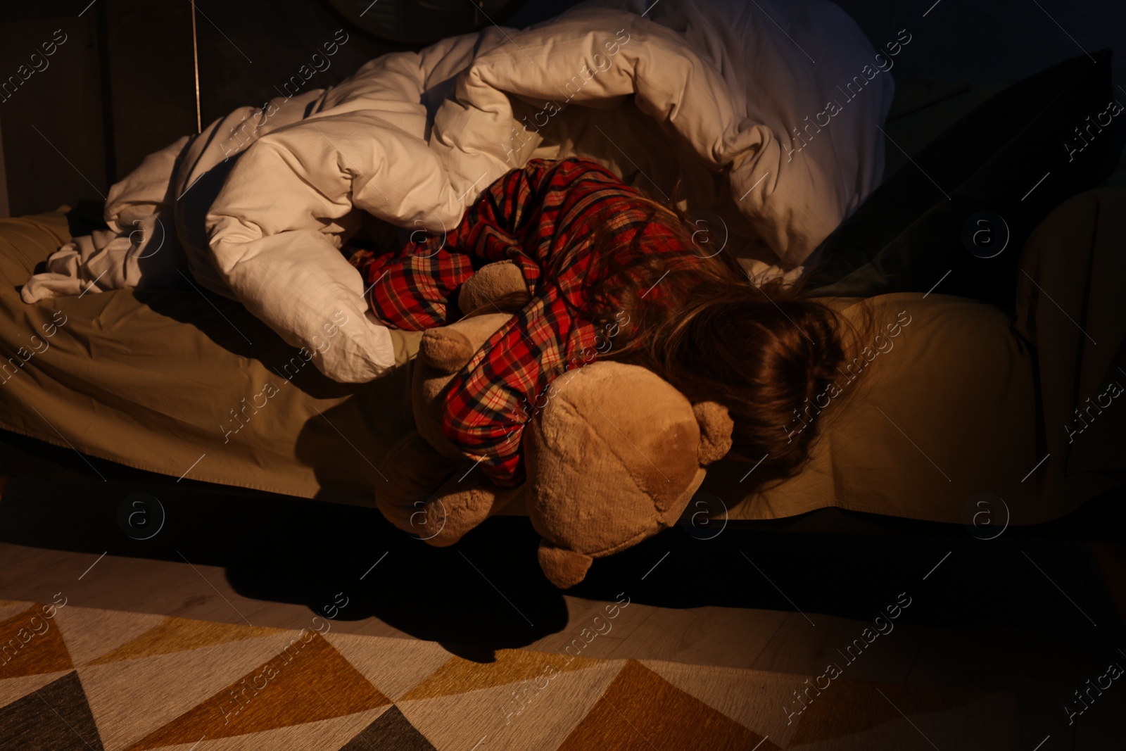 Photo of Little girl with toy looking for monster under bed at night