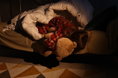 Little girl with toy looking for monster under bed at night