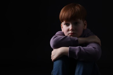 Portrait of sad little boy on black background, space for text