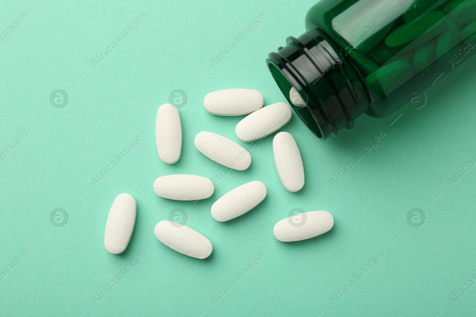 Photo of Vitamin pills and bottle on mint color background, top view