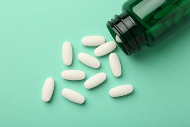 Photo of Vitamin pills and bottle on mint color background, top view