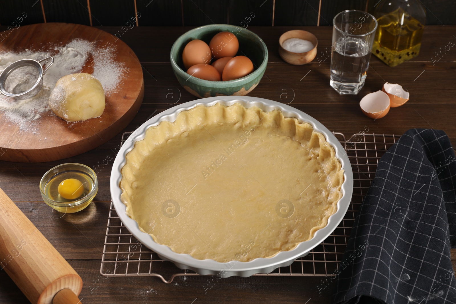 Photo of Pie tin with fresh dough, rolling pin and ingredients on wooden table. Making quiche