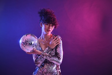 Photo of Beautiful young woman with disco ball posing on color background in neon lights. Space for text