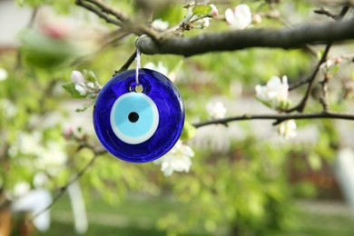 Photo of Evil eye amulet hanging on blossoming spring tree outdoors, closeup. Space for text