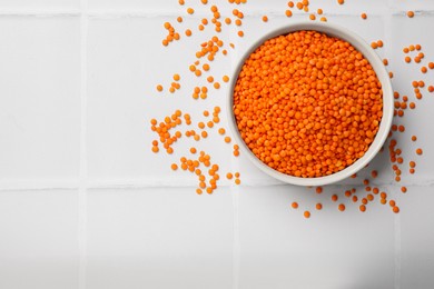 Photo of Raw red lentils in bowl on light tiled table, top view. Space for text