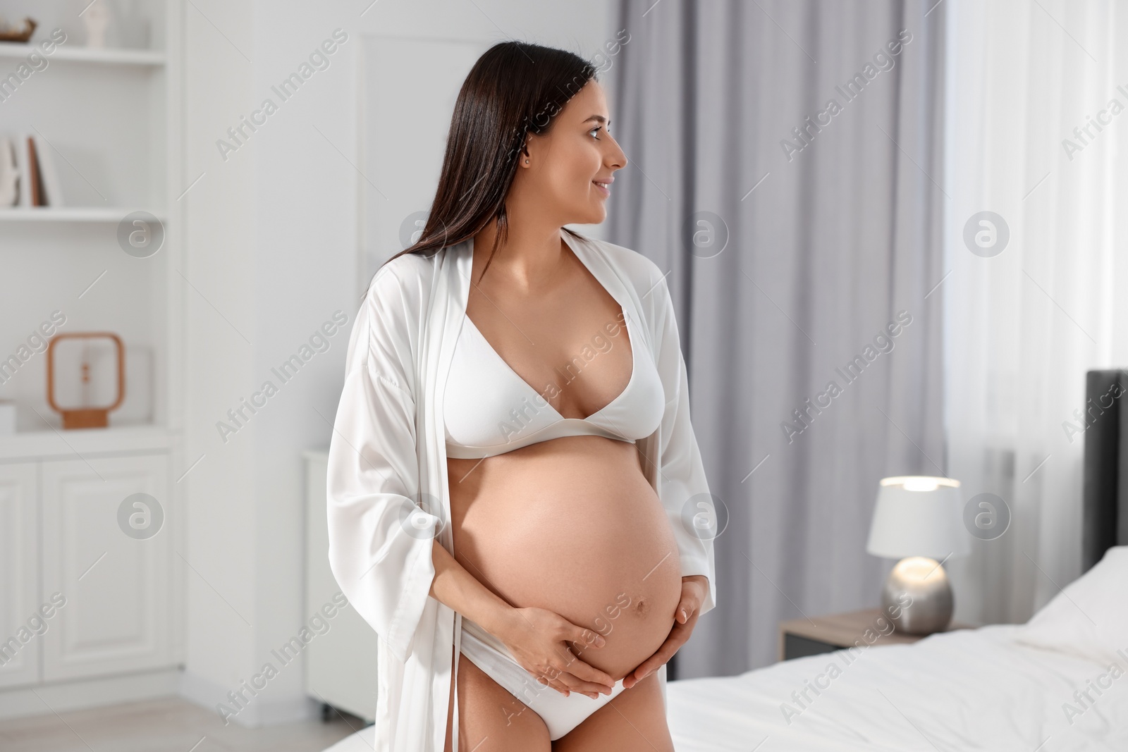 Photo of Beautiful pregnant woman wearing stylish comfortable underwear and robe in bedroom