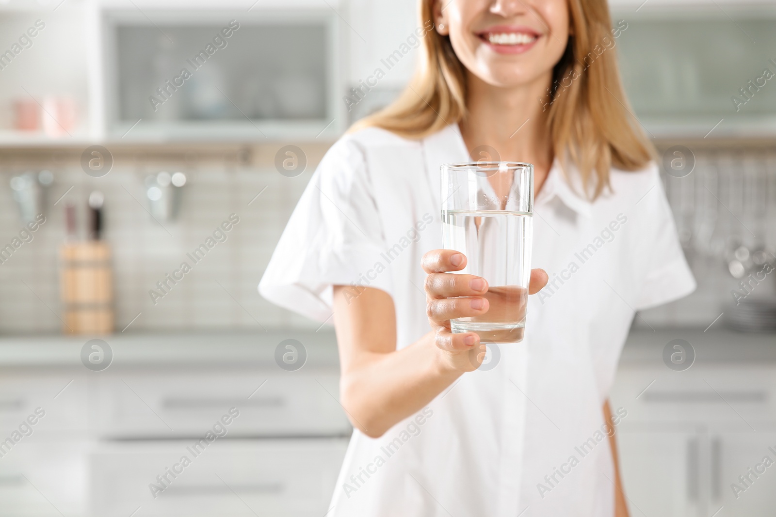 Photo of Young woman holding glass with clean water in kitchen, closeup