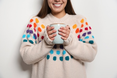 Beautiful young woman in warm sweater with cup of hot drink on white background