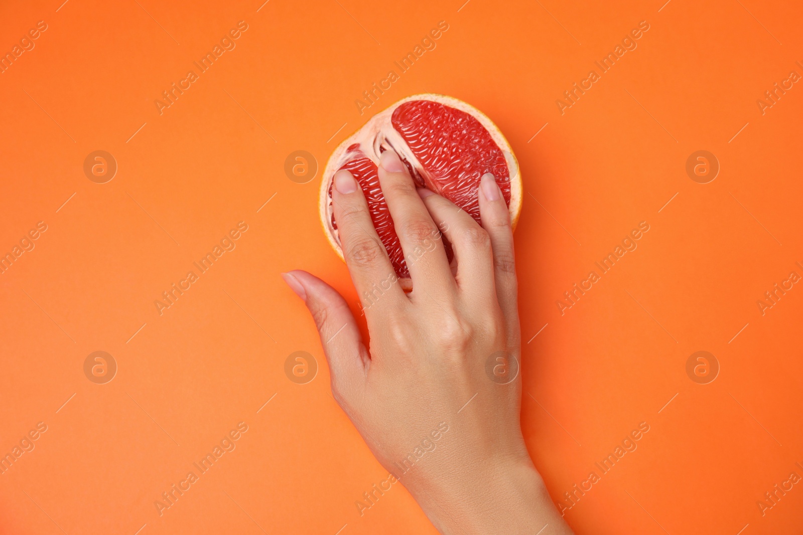 Photo of Young woman touching half of grapefruit on orange background, top view. Sex concept