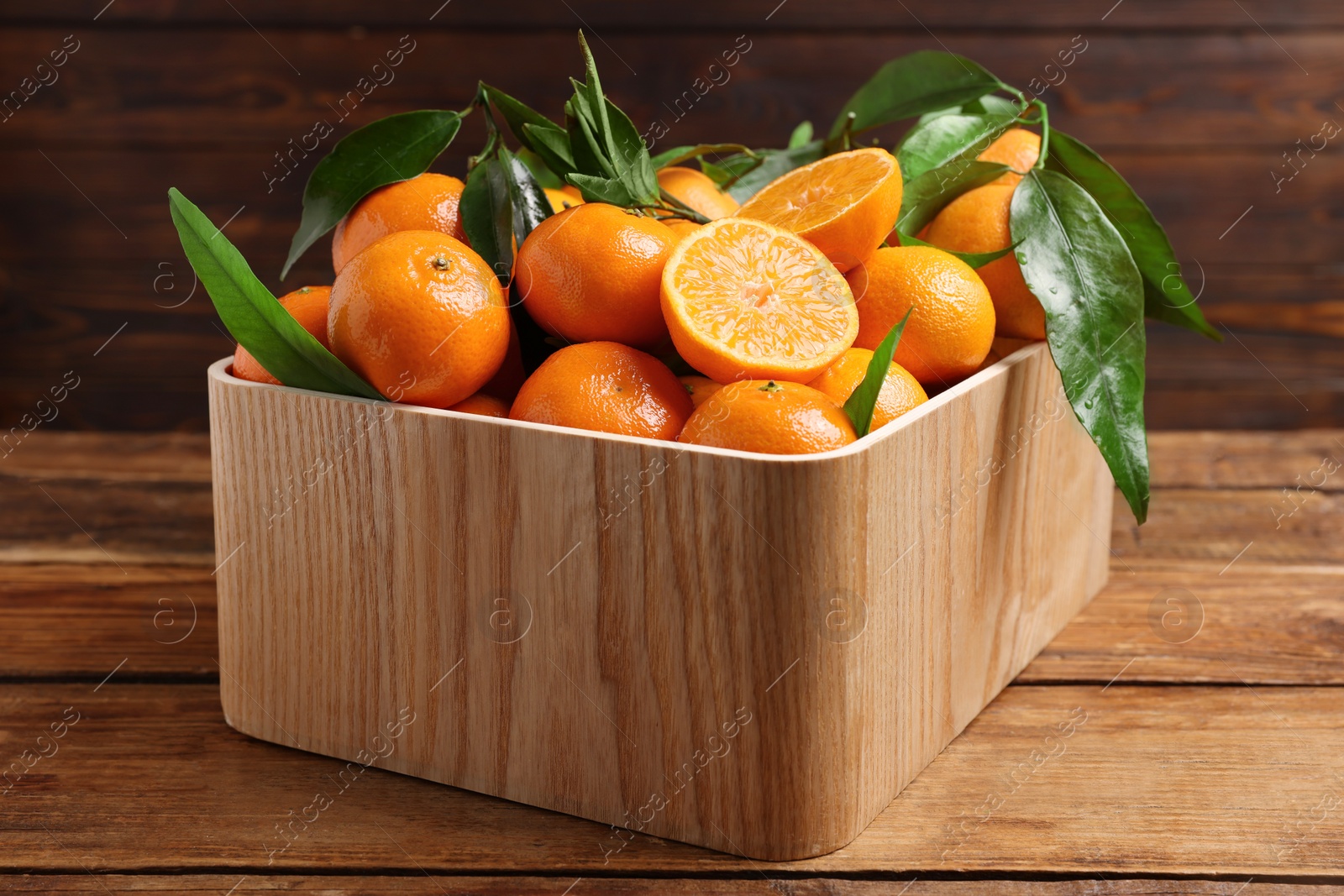 Photo of Fresh tangerines with green leaves in crate on wooden table