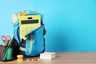 Backpack and different school stationery on wooden table against light blue background, space for text