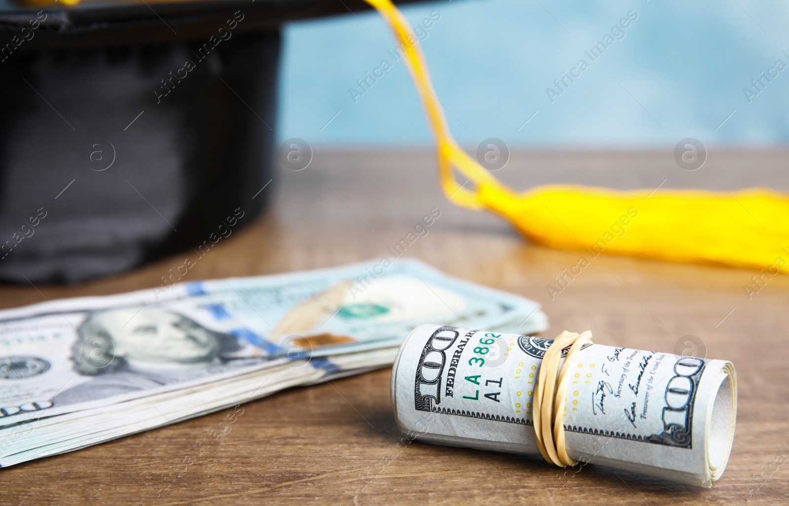 Photo of Dollar banknotes and student graduation hat on wooden table against blue background. Tuition fees concept