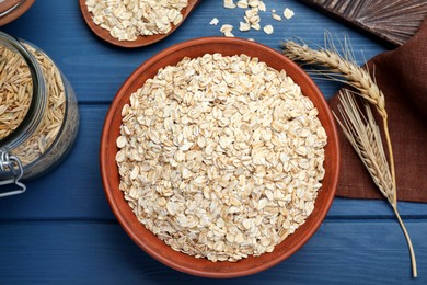 Photo of Bowl of oatmeal and spikelets on blue wooden table, flat lay