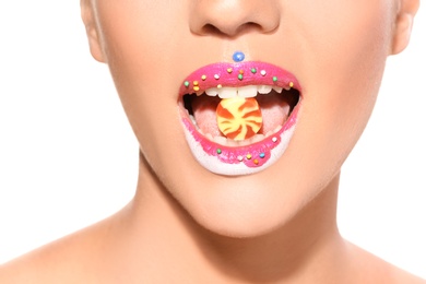 Photo of Beautiful young model with creative makeup holding candy in lips on white background